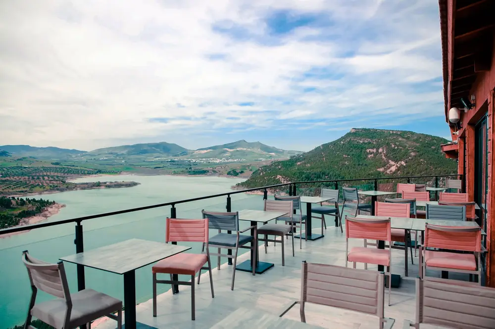 Leere Terrasse mit Tischen und Stühlen an einem See vor Bergen